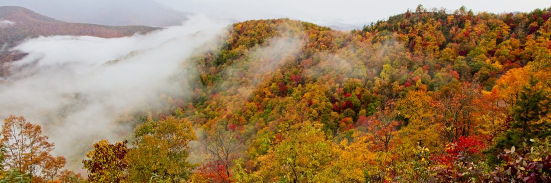 Fog pouring through a valley of fiery red, orange, and gold autumn ridgelines