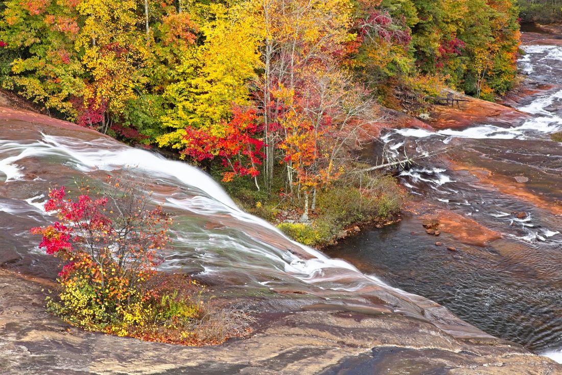 River sliding over smooth granite slabs beside brilliant red and gold autumn trees