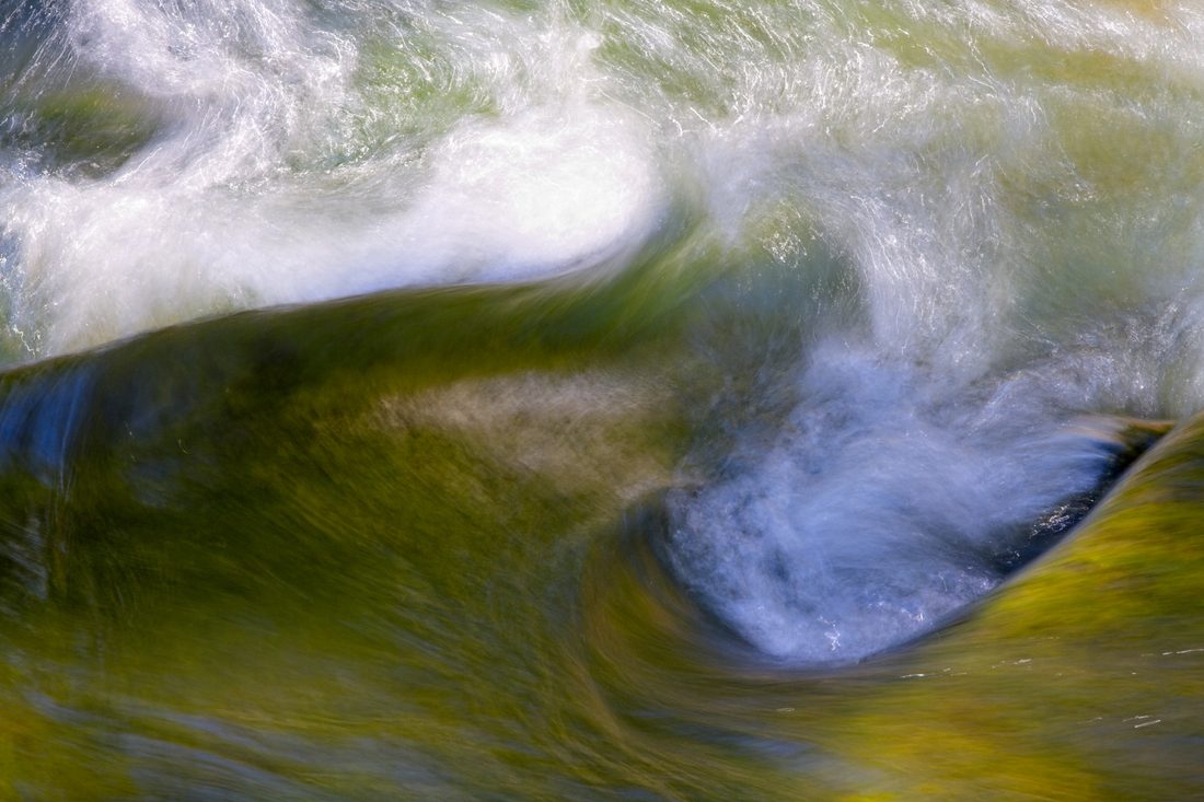 Abstract close-up of swirling green and white river current with painterly motion